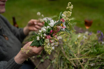 hands making flower wreath with wildflowers and greenery, summer craft activity, midsummer...