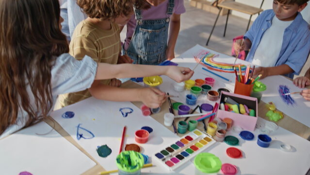 Creative school children painting at art lesson on classroom desk. Group pupils