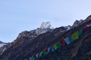 Colorful prayer flags flutter in the foreground while the majestic peak of Machapuchare or Fish...