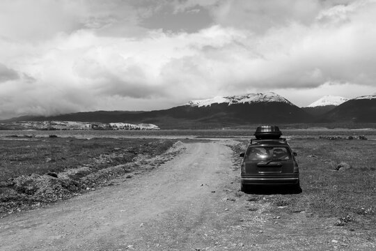 Imagem em preto e branco de um carro de passeio parado ao lado de uma estrada de frente para o Canal de Beagle