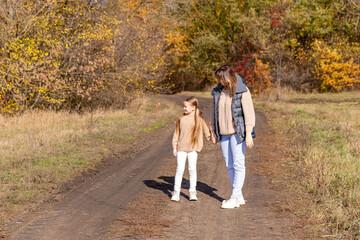 Fototapeta premium Mother walking and holding hands with daughter for bonding, outdoor adventure or journey in nature. Mom strolling with child little girl on sidewalk in autumn season at park. Happy family concept