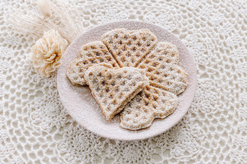 Freshly baked, homemade heart waffles with powdered sugar on a white crochet tablecloth, vintage, minimalistic, scandinavian 