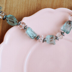 Chunky silver earrings with raw crystals and matching bracelet with clear and aqua stones on pink ceramic plate, wooden background. Concepts: handmade jewelry, accessories, elegance, gift idea.