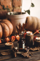 Autumn cozy mood composition with burning candles. Aroma stick reed diffuser, pumpkin on wooden table, knitted warm plaid. Fall hygge home decor, aromatherapy. Relaxed atmosphere in the apartment