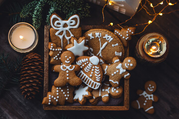 Concept of home christmas or new year celebration, family traditions. Assortment of gingerbread cookies with icing in a vintage wooden box on a window sill with atmospheric lights