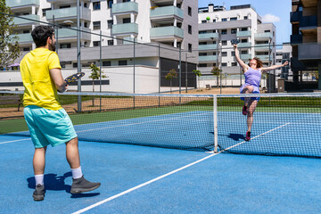 Woman jumping and smashing ball during pickleball training with coach on a sunny day