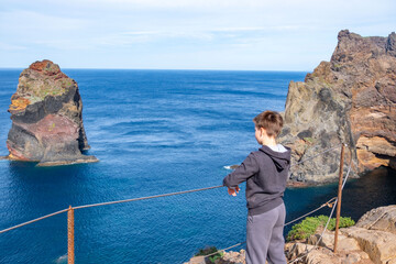Young boy stands on volcanic cliff edge Madeira island, hiking adventure, cliffside trail, gazing...