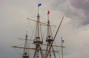 Masts and flags of an ancient ship against a cloudy sky