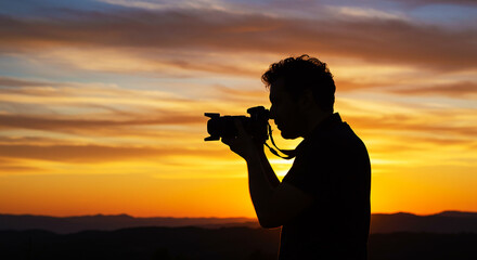 Silhouette of photographer holding camera against a vibrant sunset landscape with cloudy skies