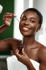 Woman applying facial serum while smiling in a serene bathroom setting during self-care routine