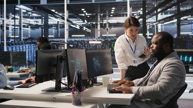 Lead data center admin overseeing IT expert integrating AI in equipment rigs. African american employee under server farm team leader supervision using deep learning for operational tasks, camera A
