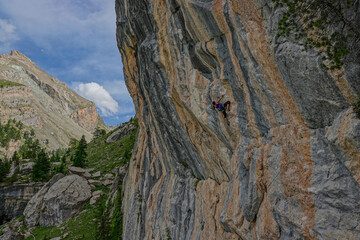 Female climber climbing up a picturesque rock face surrounded by rugged peaks and lush greenery....