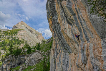 Focused climber ascends a layered rock face in a dramatic mountain landscape under blue sky with...