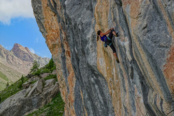 LOW ANGLE VIEW: Climber on a difficult section of a streaked, layered rock face. Stunning alpine mountain backdrop provides a magnificent setting for this demanding yet rewarding athletic endeavour.