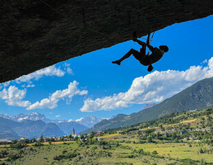 SILHOUETTE: Skilled male rock climber hanging from a rocky overhang with the expansive alpine...