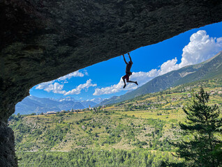 SILHOUETTE: Shirtless sport climber hangs from an overhang, framed against a brilliant blue sky...
