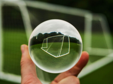 Football or soccer goal posts in glass ball which is hold by a someone hand. Forecasting sport results in popular world sport. Betting on club and national teams concept. Selective focus.