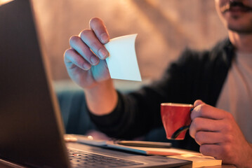 Close up of a man working late on a laptop in a modern interior with ambient light, holding a...