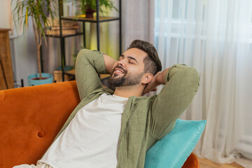 Tired Caucasian handsome man enjoy relaxing on home sofa in living room. Happy guy lying on couch...