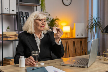 Sick upset senior businesswoman grandmother working on laptop computer suffering from headache at...