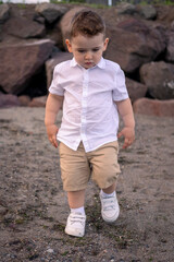 Child enjoying a quiet beach afternoon. little boy walking on the beach. Curious boy in white shirt walks along the shore.