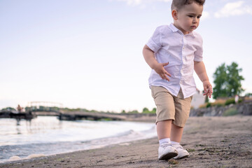 young boy running on the beach. Child enjoying a quiet beach afternoon. little boy walking on the beach. Curious boy in white shirt walks along the shore.