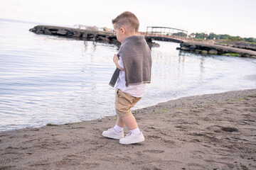 A boy stands quietly, looking out to sea.. Boy looking out to sea. A little boy and a giant sea.