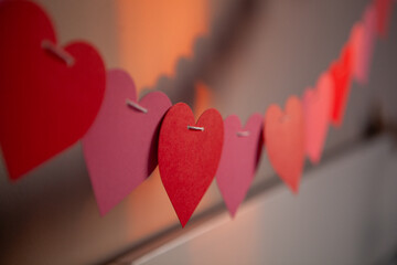 Colorful paper hearts in shades of red and pink are strung along a wall, creating a festive...