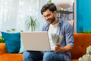 Planning budget. Rich happy Indian man counting money cash use laptop computer calculate domestic...