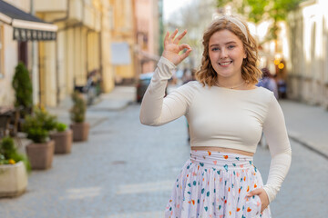 Okay. Happy cheerful redhead young woman in long dress looking approvingly at camera showing ok...