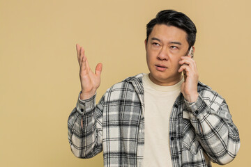 Disinterested Asian man having annoyed boring talk on smartphone. Chinese guy tired sleepy freelancer talking on mobile phone with friend, making online conversation isolated on beige background