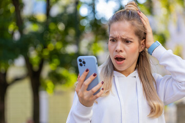 Caucasian young woman using smartphone typing browsing, loses becoming surprised sudden lottery...