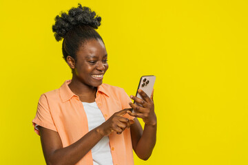 African American woman holds smartphone, scrolling social media with engaged focus, occasionally...