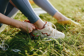 Female athlete tying shoelaces in a grassy field, wearing sporty clothing, showcasing focus and determination in a vibrant outdoor setting