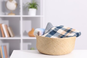 Stylish wool scarves in wicker basket on white table indoors