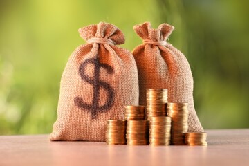 Burlap bags and stacked coins on table against blurred background