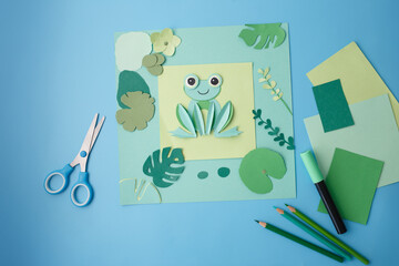 Green paper frog in quilling style on colored sheet, top view. Perfect for kids activity books, DIY craft tutorials, early learning games, creative workshop ads, educational packaging.