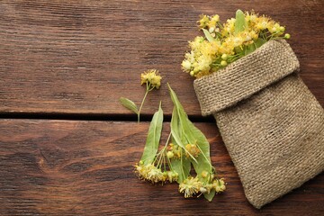 Branches with linden flowers, green leaves and sack on wooden table, flat lay. Space for text