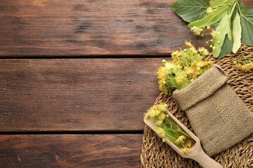 Branches with linden flowers, green leaves, scoop and sack on wooden table, flat lay. Space for text
