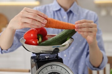 Woman weighting vegetables on kitchen scale indoors, closeup