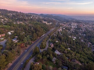 Aerial view of cars commuting on Warren Freeway through wooded hills at sunset in Oakland,...