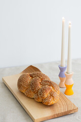 sesame seed challah bread on wooden board on table with two shabbat candles in colorful holders