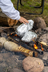 Campfire cooking with food wrapped in aluminum foil over open flames