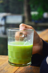 Close-up image of a woman holding a cup of hot matcha green tea relaxing beside on the lake