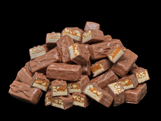 Pile of chocolate candy bars with caramel and peanuts on black background