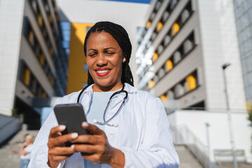 african american woman doctor on break use cellphone in front hospital