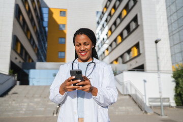 african american woman doctor on break use cellphone in front hospital