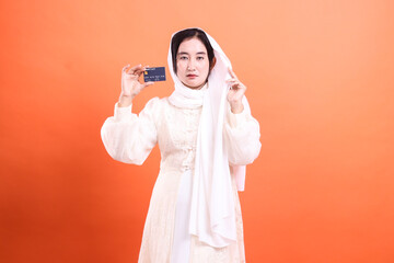 Muslim woman in hijab showcases her debit card, isolated on a orange background, promoting secure...