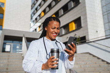 african american woman doctor on break use cellphone in front hospital