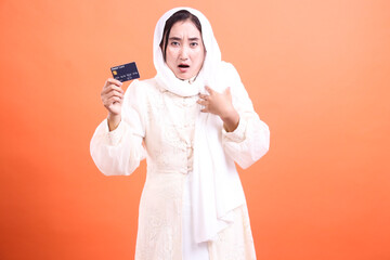 Worried Muslim woman holding a debit card, feeling anxious about overspending and potential...